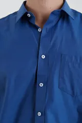 Camisa azul de manga larga con cuello clásico, cierre con botones y bolsillo en el pecho.