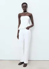 Top blanco estilo palabra de honor con corte peplum en la cintura. Diseño sin mangas y entallado en el torso.