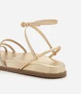 Sandalia plana color dorado con acabado metalizado, diseño de tiras finas, algunas de ellas con incrustaciones de brillo, y cierre ajustable con hebilla al tobillo.