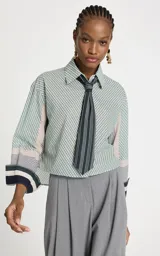 Camisa de algodón con estampado de rayas diagonales en tonos verdes y beige, corte recto y amplio. Presenta cuello clásico estructurado, mangas largas con puños anchos y cierre frontal de botones. Incluye una corbata a juego con rayas verticales en contraste.