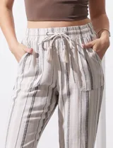 Pantalón de lino color beige con rayas verticales grises, corte recto, cintura alta con cordón ajustable y bolsillos laterales.