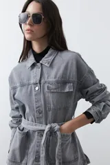 Sobrecamisa de jean color negro con silueta relajada, cuello camisero, cierre frontal con botones metálicos, bolsillos frontales y cinturón ajustable en la cintura.