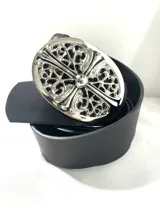 Cinto de cuero sintético negro con una gran hebilla metálica plateada de forma ovalada, con diseño ornamental y una cruz en relieve calada.