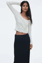 Remera ajustada de manga larga en punto acanalado blanco, con escote cuadrado ribeteado en encaje y un pequeño moño de satén en el centro del escote.