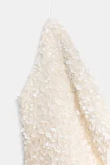 Top blanco con lentejuelas, cuello halter y escote fluido.