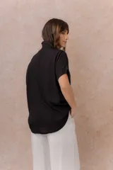 Camisa negra de calce amplio y relajado, confeccionada en tejido liviano con textura sutil. Cuenta con diseño oversize, hombros caídos, mangas cortas amplias, cuello camisero y abotonadura frontal con botones claros.