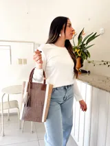 Bolso matero de cuero color taupe con textura croco y detalles en cuero color marrón. Tiene doble asa de mano y un dije de borla.