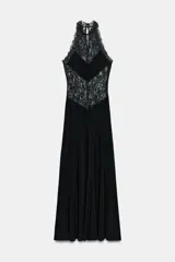 Vestido largo negro de cuello halter con detalles de encaje en la parte superior y espalda. Cuenta con corte en línea evasé y cierre posterior con abertura y botón.