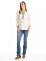 Blusa de tejido crepé color blanco, con mangas tres cuartos y silueta evasé. Presenta un panel frontal con encaje calado y bordados geométricos en tonos verdes y azules alrededor del escote en V.