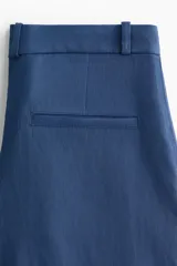 Pantalón sastrero de tiro alto y perneras amplias en color azul, con pinzas delanteras y traseras marcadas, y trabillas para cinturón.