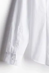 Camisa de vestir blanca con cuello inglés, tapeta clásica y corte ajustado. Presenta mangas largas con puños abotonados y bajo levemente redondeado.
