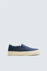 Zapatilla tipo slip-on de lona azul marino, con elástico lateral para facilitar el calce y suela de goma color crema.