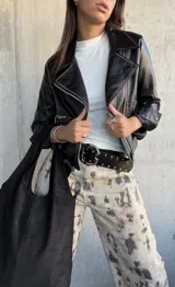 Chaqueta tipo biker de cuero vegano color negro, con solapas amplias, cierre frontal cruzado y detalles de cierres metálicos en los bolsillos y puños.