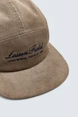 Gorra de cinco paneles confeccionada en pana de algodón, con visor plano y ajuste posterior. Presenta un bordado frontal con el texto 'Lassen Field'.