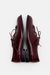 Zapato acordonado de cuero color bordó, con punta fina y diseño estilo oxford. Presenta cordones al tono y detalles de ojales metálicos dorados.