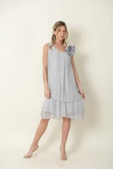 Vestido midi de seda color gris, sin mangas, con escote redondo, diseño suelto de capas con volados en el bajo y detalle de flor de tela en el hombro.
