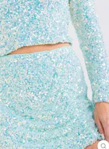 Conjunto de crop top de manga larga con hombreras y mini falda drapeada, confeccionados con tela elastizada cubierta de lentejuelas celestes.