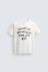 Camiseta de manga corta y cuello redondo, color blanco roto con efecto lavado y desgastado. Presenta un estampado frontal en negro con texto de estilo universitario que incluye "PRINCE ST.", "GROOVE ALLEY", "SOHO, NYC" y el número "95".