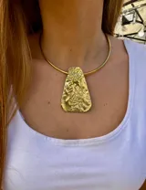 Collar rígido dorado con dije rectangular irregular con textura rugosa.