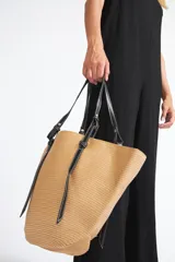 Bolso tipo shopper de paja color beige con asas de cuero sintético negro y costuras blancas.