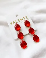 Par de aros colgantes con tres piedras rojas en forma de gota engarzadas en metal plateado.