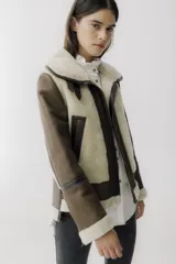 Campera tipo gamulán de cuero negro con interior y detalles en piel sintética negra, cierre frontal y cuello con hebillas ajustables.