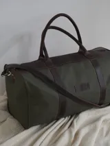 Bolso de lona color verde militar con detalles en cuero marrón. Tiene doble asa de mano y correa de hombro ajustable y extraíble.