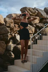 Vestido corto negro de lino y rayón, con escote recto, breteles regulables y diseño cut-out en la cintura.