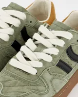 Championes Coolway modelo Goal, color verde musgo, confeccionados en serraje suave con detalles en contraste de color. Cuentan con lengüeta preformada de piel acolchada, forro interior en piel, cordones planos de algodón bicolor intercambiables, cuello ligeramente acolchado, puntera reforzada con pespuntes decorativos y suela flexible de goma y caucho.