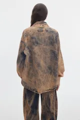 Camisa de denim oversize, con efecto acid wash en tonos marrones y negros, mangas abullonadas, cuello en V con solapa y bolsillos frontales con solapa.