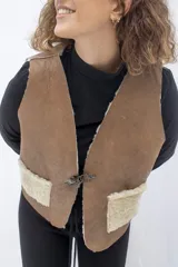 Chaleco reversible confeccionado en cuero genuino. Presenta un lado de piel de oveja gris con bolsillos de cuero negro y un lado de cuero liso gris. Diseño sin mangas con cierre frontal.