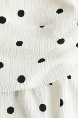 Top halter color blanco con estampado de lunares negros, escote en V pronunciado y detalle fruncido en la cintura con vuelo tipo peplum.