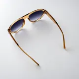 Lentes de sol tipo aviador con armazón negro de policarbonato y detalles metálicos dorados en las patillas. Lentes oscuros con filtro UV400.