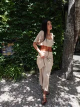 Vestido largo de dos piezas, compuesto por un top y una falda larga con volados. El conjunto es de color beige claro, con textura plisada y un cinturón ancho de cuero marrón que marca la cintura.