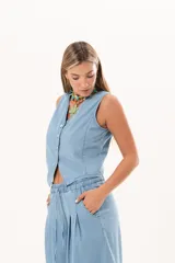 Chaleco de denim fino y liviano color celeste, con silueta entallada, escote en V y cierre frontal con botones de nácar. Presenta un diseño sastrero con terminación en puntas en la delantera.