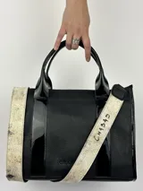 Bolso tote negro de cuero con detalles de charol, doble asa corta y correa bandolera de tela con letras.