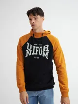 Canguro negro y ocre con capucha y cuello en rib, manga raglán, bolsillos laterales y estampa combinada (estampa y bordado).