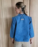 Blusa blanca de manga larga con cuello alto y volados en cuello y hombros.