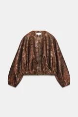 Chaqueta estilo bomber de cuello redondo y manga larga, confeccionada en tejido jacquard con acabado metalizado brillante. Presenta diseño con pliegues y cierre frontal con cremallera.