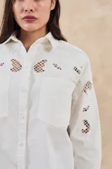 Sobrecamisa blanca de algodón con bordados florales calados en mangas, cuello y pechera. Corte oversize, manga larga y dos bolsillos frontales.