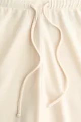 Pantalón de punto fino color beige, de corte relajado con piernas rectas y cintura elástica con cordón ajustable.
