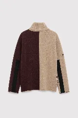 Polera de tejido lambswool con diseño bicolor en tonos neutros. Presenta cuello alto tejido, mangas largas con franjas laterales en color marrón y detalle de bordado artesanal con tres pequeñas líneas horizontales en colores vibrantes.