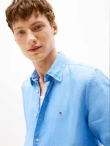 Camisa de manga larga color celeste, confeccionada en lino con un acabado pigmentado. Presenta cuello clásico, cierre frontal de botones y el logo de Tommy Hilfiger bordado en el pecho.