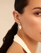 Aros colgantes de metal plateado con dos piezas circulares irregulares unidas por una argolla.