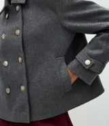 Saco corto de corte regular confeccionado en polivelour gris, con cuello inglés, cierre frontal de doble abotonadura con botones dorados y mangas largas con detalle de trabas en los puños.