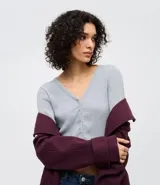 Cardigan de punto texturizado color rosado, con escote en V, cierre frontal por botones, mangas largas y acabado con volados sutiles en el ruedo y los puños.