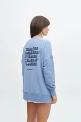Buzo celeste de corte holgado con cuello redondo y mangas largas. Estampado en la espalda con la frase "Chasing sunbeams through fields of flowers".
