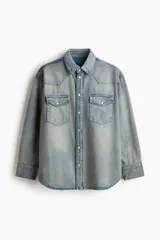 Camisa de denim de algodón rígido, de corte oversized y silueta holgada. Cuenta con cuello clásico, cierre frontal de botones a presión, canesú en la parte delantera y trasera, bolsillos con solapa en el pecho, mangas largas con puños abotonados y bajo redondeado.