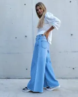 Pantalón de jean color beige, de corte recto y tiro alto, con ruedo deshilachado y cierre frontal con botón y cremallera.