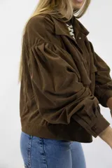 Campera corta de pana color beige, con cuello clásico, cierre frontal con botones y amplios bolsillos con solapa en el pecho. Cuenta con mangas largas abullonadas y diseño holgado.